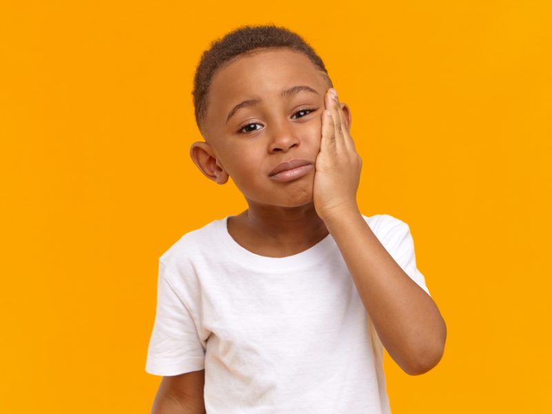 child in dental pain Young child holding cheek showing signs of toothache and dental pain