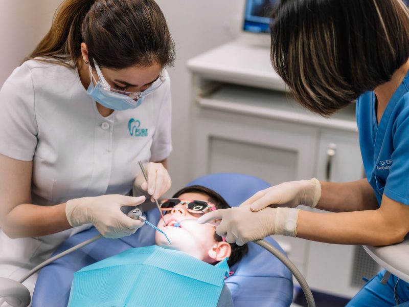 paediatric-dental-treatment-child-clinic Child receiving dental treatment from two paediatric dentists in a clinic setting