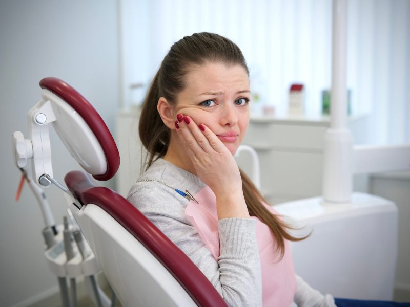 woman at the dentist holding her cheeck due to dental pain